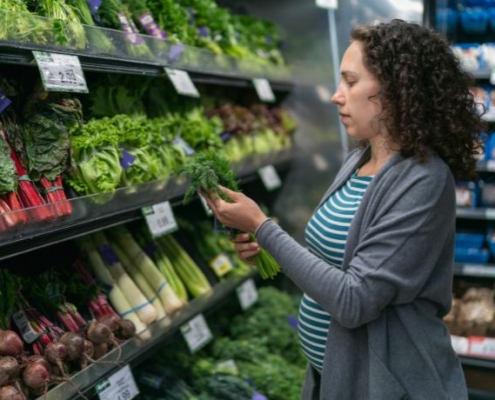 A woman inspects fresh herbs in a grocery store produce department