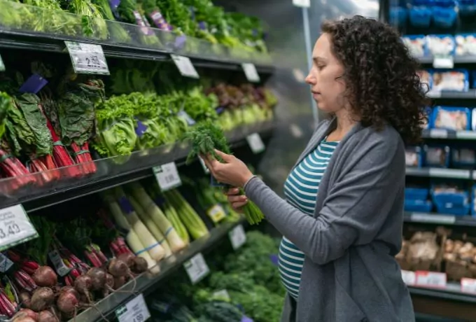 A woman inspects fresh herbs in a grocery store produce department